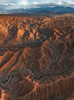 River bed runs through a landscape of eroded hills, badlands at sunset, mountain peaks of the Tian