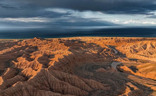Riverbed runs through a landscape of eroded hills, badlands at sunset, Issyk Kul Lake in the