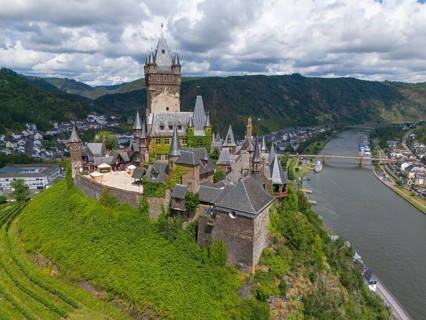 Medieval castle on a hill overlooking a river and a town, embedded in green nature and surrounded