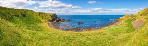 Green meadows meet the coast with a view of the sea under a blue sky, Giant Causeway