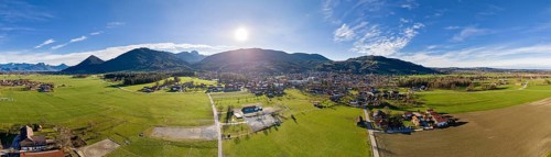 Aerial view of a village in a mountainous landscape under a bright blue sky, Bad Feilnbach