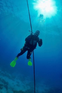 Diver making a safety stop in deep blue water with the sun shining above her. Dive site Punta