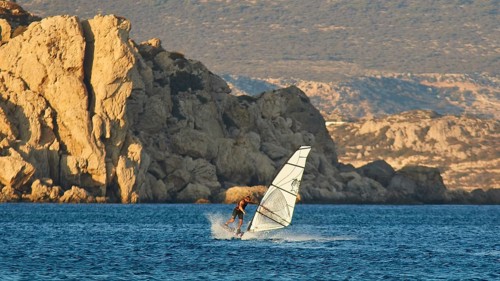 A windsurfer navigates past large rock formations, windsurfer, Meltemi windsurfing spot, Devils