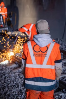 Worker in safety waistcoat observing welding work with sparks in the tunnel, rail welding, track