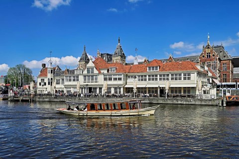 Boat with tourists on a canal, behind a steakhouse and the Centraal Station, Amsterdam, Netherlands