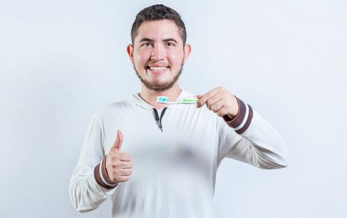 Happy man showing toothbrush with toothpaste gesturing OK. Handsome man holding brush with OK