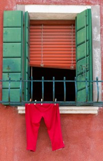Half open window with green shutters and red trousers hanging in front of it, Burano, Venice,