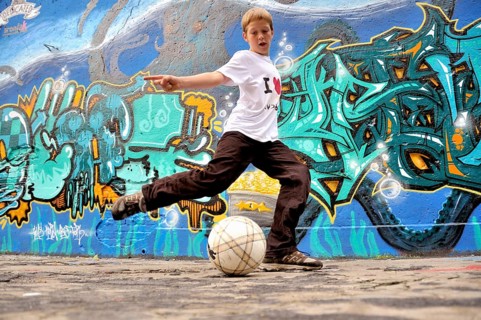 A ten-year-old boy plays with his football in front of a graffiti wall, football pitch in Germany