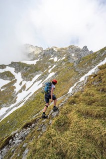 Mountaineer with helmet on a narrow hiking trail, ascent to the Ackerlspitze, clouds moving around