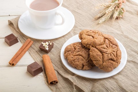 Homemade oatmeal cookies with a cup of cocoa on a linen textile and white wooden background. side