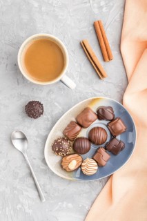 Different chocolate candies and a cup of coffee on a gray concrete background and orange textile.
