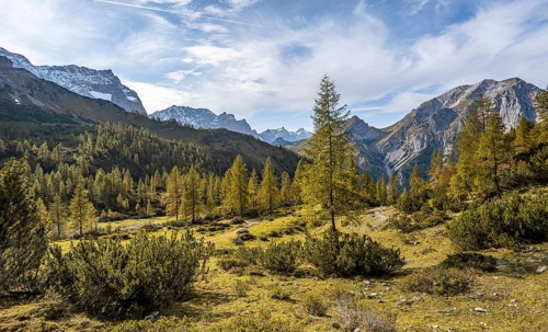 Mountain panorama with steep rocky peaks, yellow-coloured larches in autumn, hike to the summit of
