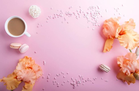Orange iris flowers and a cup of coffee on a pink pastel background. Morninig, spring, fashion