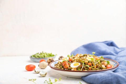 Mung bean porridge with quail eggs, tomatoes and microgreen sprouts on a white concrete background