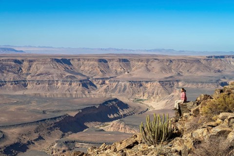 Woman sitting on a rock on the edge of the precipice in front of the gorge landscape of the Fish