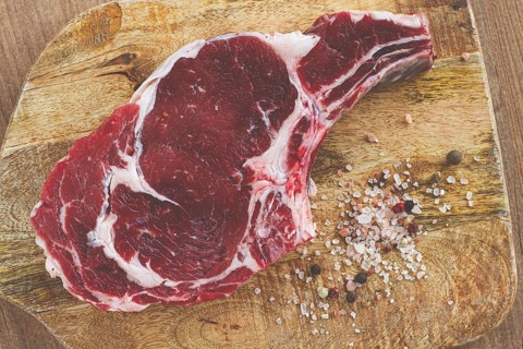 Raw rib eye steak, cowboy steak, on a wooden chopping board, top view, no people