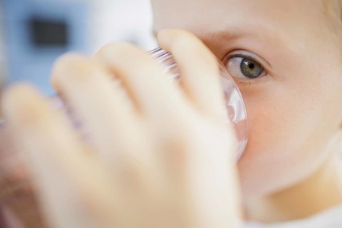 Symbolic photo on the subject of drinking water in high temperatures. A boy drinks a glass of water