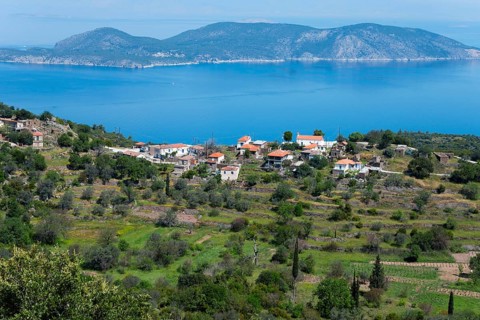 Coastal landscape with traditional houses and hills surrounded by blue sea and green vegetation,