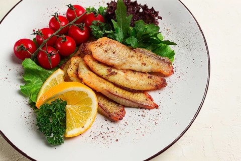 Fried Tilapia fish fillet, in spices, with cherry and salad, on a white plate, homemade, no people