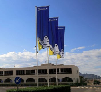 Company flags with logo Bibendum figure flying outside, Michelin factory and research