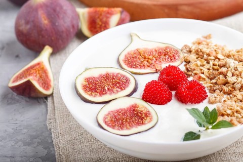 Yoghurt with raspberry, granola and figs in white plate on a gray concrete background and linen