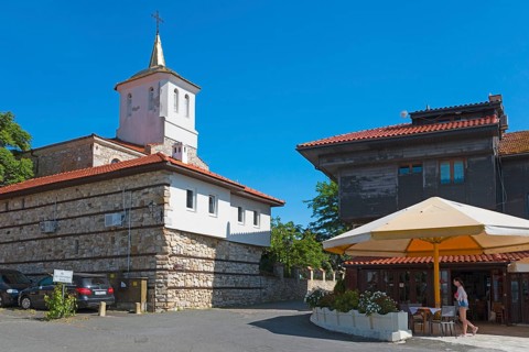 Historic church under clear blue sky next to urban buildings with people and parked cars, Orthodox