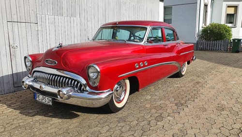 A shiny red classic car with chrome details parked in front of a white garage door, classic car,