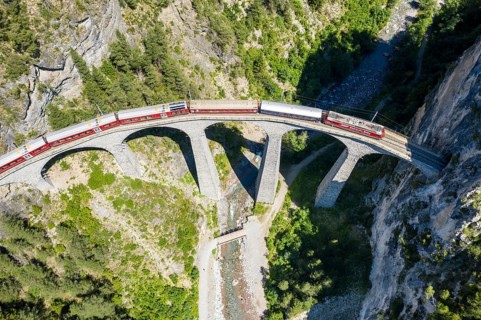 Drone shot of train passing the Landwasserviadukt near Filisur, red train of Bernina Express,
