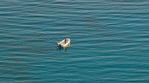 Single boat with one person on calm blue sea in the distance, Anthony Quinn Bay, Vagies Bay,