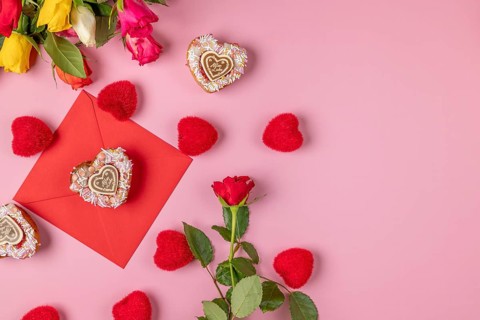 Valentine's Day composition with roses, hearts and envelope, heart-shaped cupcakes, on a pink