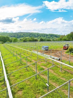 Metal frames of a solar park under construction in a rural area, surrounded by forests and under a