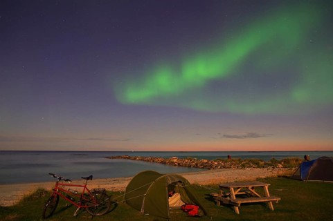 Green northern lights and stars in the sky above a beach with tent and bicycle at night, Bleik,