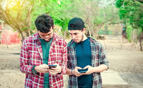 Jealous friend spying on his friend's cellphone outdoors, Friend spying on his friend phone. A guy