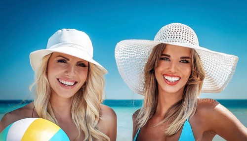 Two young woman in sun hats playing with a beach ball on the beach in the Caribbean