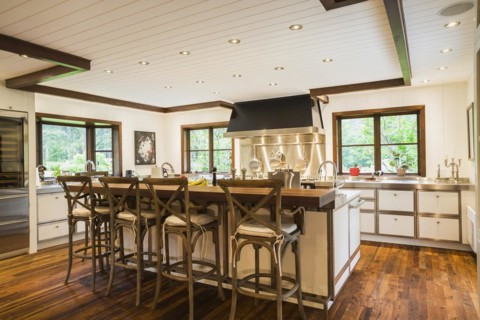 Country style kitchen with island and rustic wooden high chairs inside a New Hampton style home,