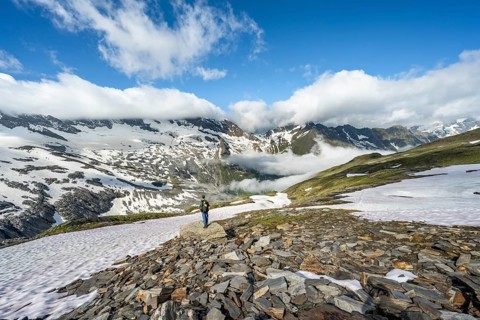 Mountaineer in front of mountain landscape with snow fields and high fog in the valley, in the