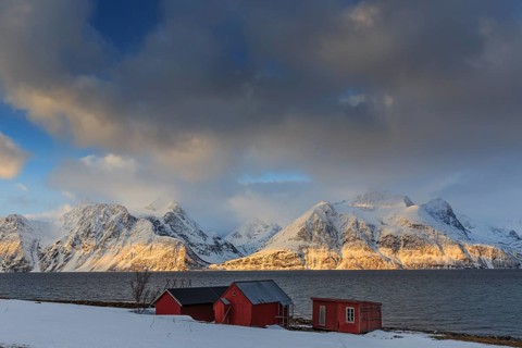 Red boathouses, coast, snowy mountains, fjord, morning light, clouds, snow, Lyngen Alps, Norway,
