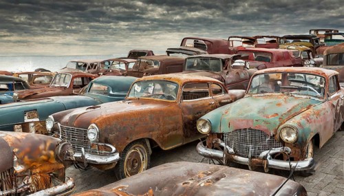 Row of abandoned, rusted cars in a large junkyard under a cloudy sky, symbolic photo, AI generated,