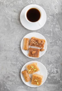 Traditional arabic sweets (basbus, kunafa, baklava) on white plate and a cup of coffee on a gray