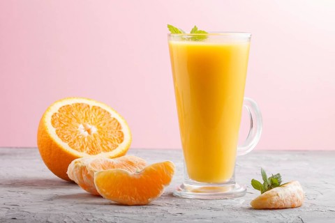 Glass of orange juice on a gray and pink background. Morninig, spring, healthy drink concept. Side