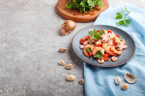 Boiled shrimps or prawns and small octopuses with herbs on a blue ceramic plate on a gray concrete