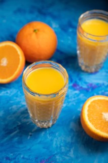 Glass of orange juice on a black and blue background. Hard light, contrast. Side view, close up