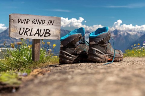 Symbolic image of company holidays/summer holidays: Hiking boots in front of an alpine backdrop and