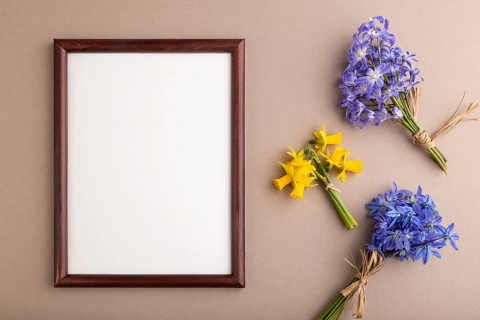 Wooden frame with spring snowdrop flowers bluebells, narcissus on beige pastel background. top