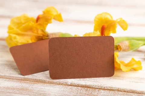 Brown business card with iris yellow flowers on white wooden background. side view, copy space,