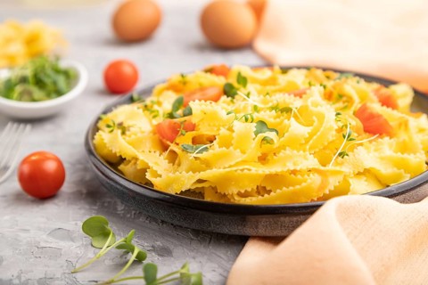 Reginelle semolina pasta with tomato, eggs and microgreen sprouts on a gray concrete background and