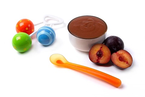 Baby food, plum puree, on a white background, with a spoon and a rattle, horizontal, no people, top