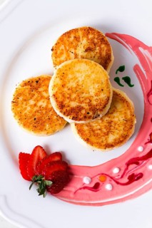 Cottage cheese pancakes, on a white plate decorated with sauce, fresh strawberry berry, close-up,