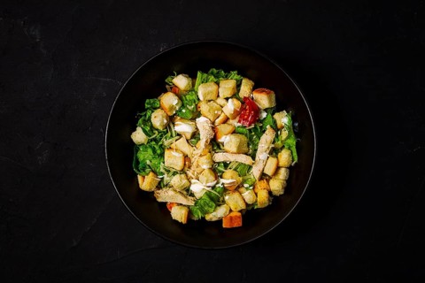 Fresh traditional Caesar salad, with chicken, on a black background, Top view, dark background,