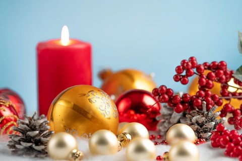 Christmas decorations with red and gold baubles, a burning candle and pine cones against a blue